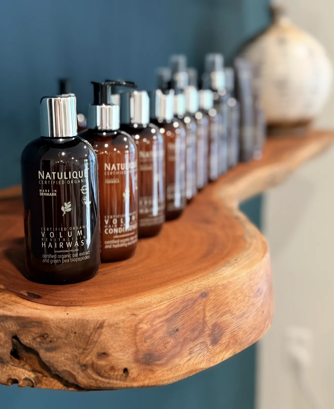 Natulique certified-organic hair care line on a live-edge wood shelf inside Vista Beauty Bar